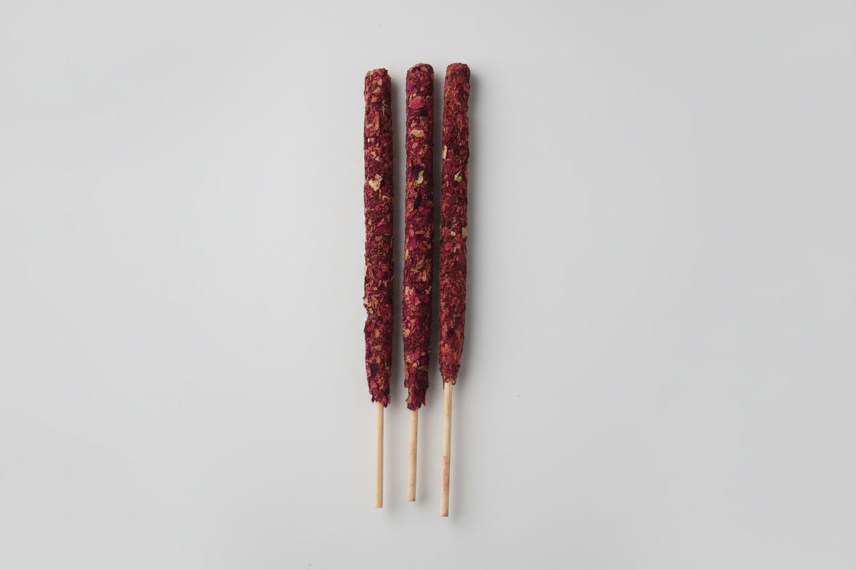 A rose smudge stick, used for spiritual practices to promote harmony and prosperity, shown partially burned with ash collected in a white bag.