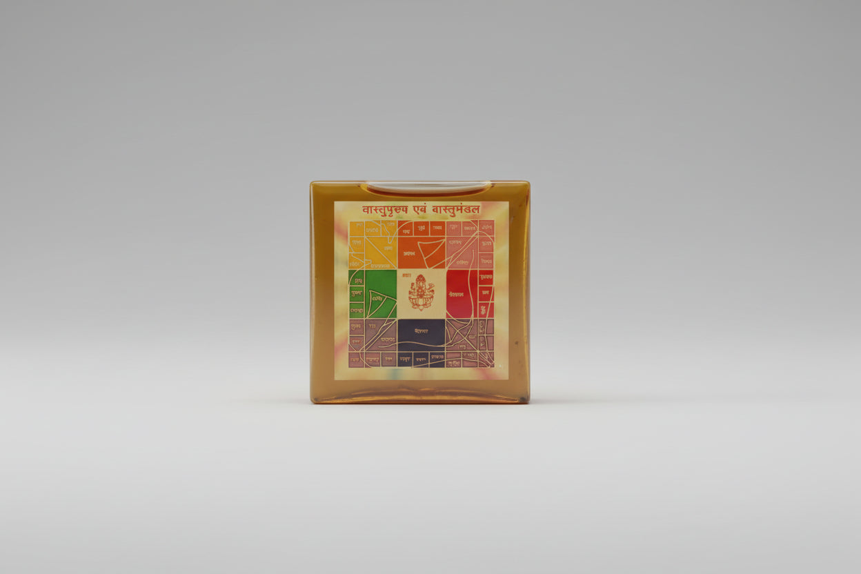 A Vastu Purush and Vastu Mandal Yantra, which is a colorful geometric pattern on a square piece of paper, held between fingers.