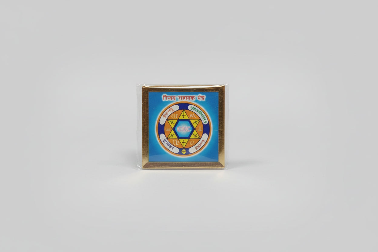 A hand holding a small yantra or spiritual symbol wrapped in plastic, with a decorative pattern predominantly in blue.