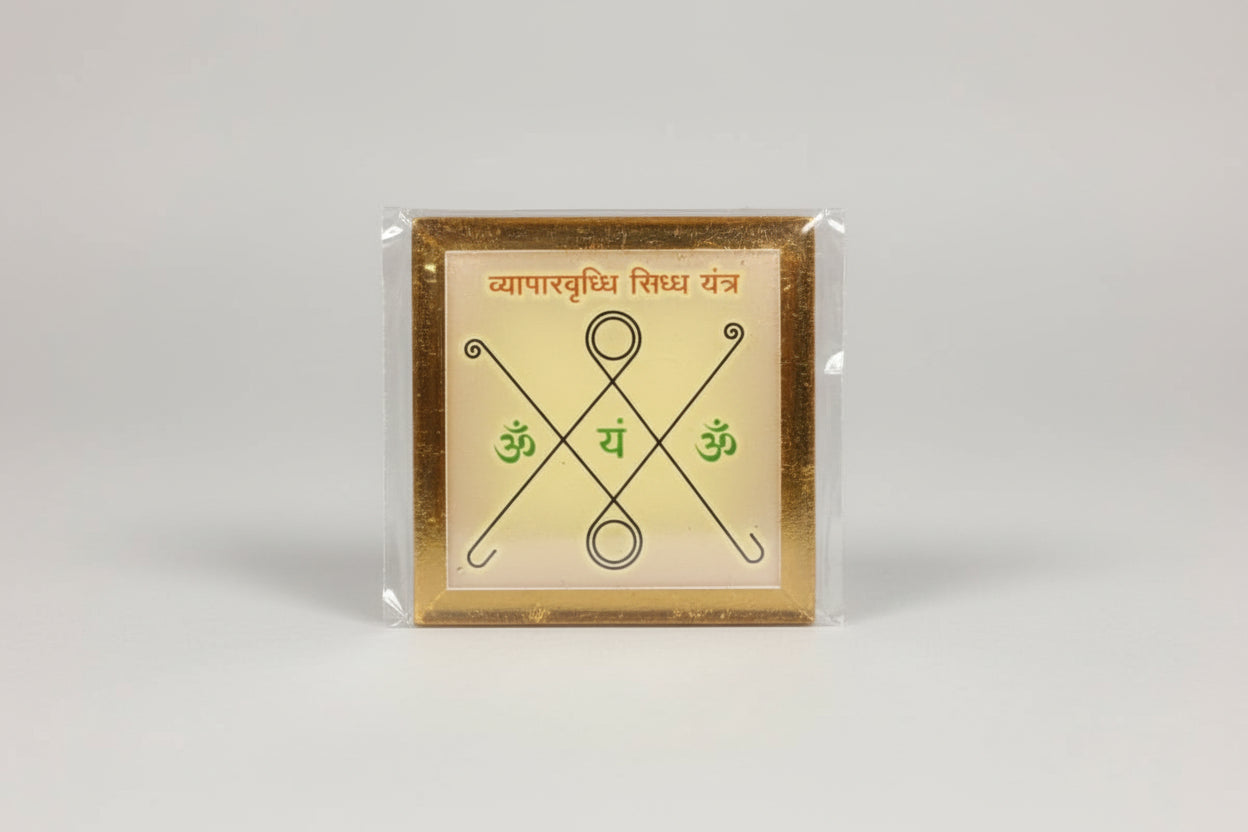 A hand holding a small, square-shaped yantra with geometric patterns and Devanagari script on it.