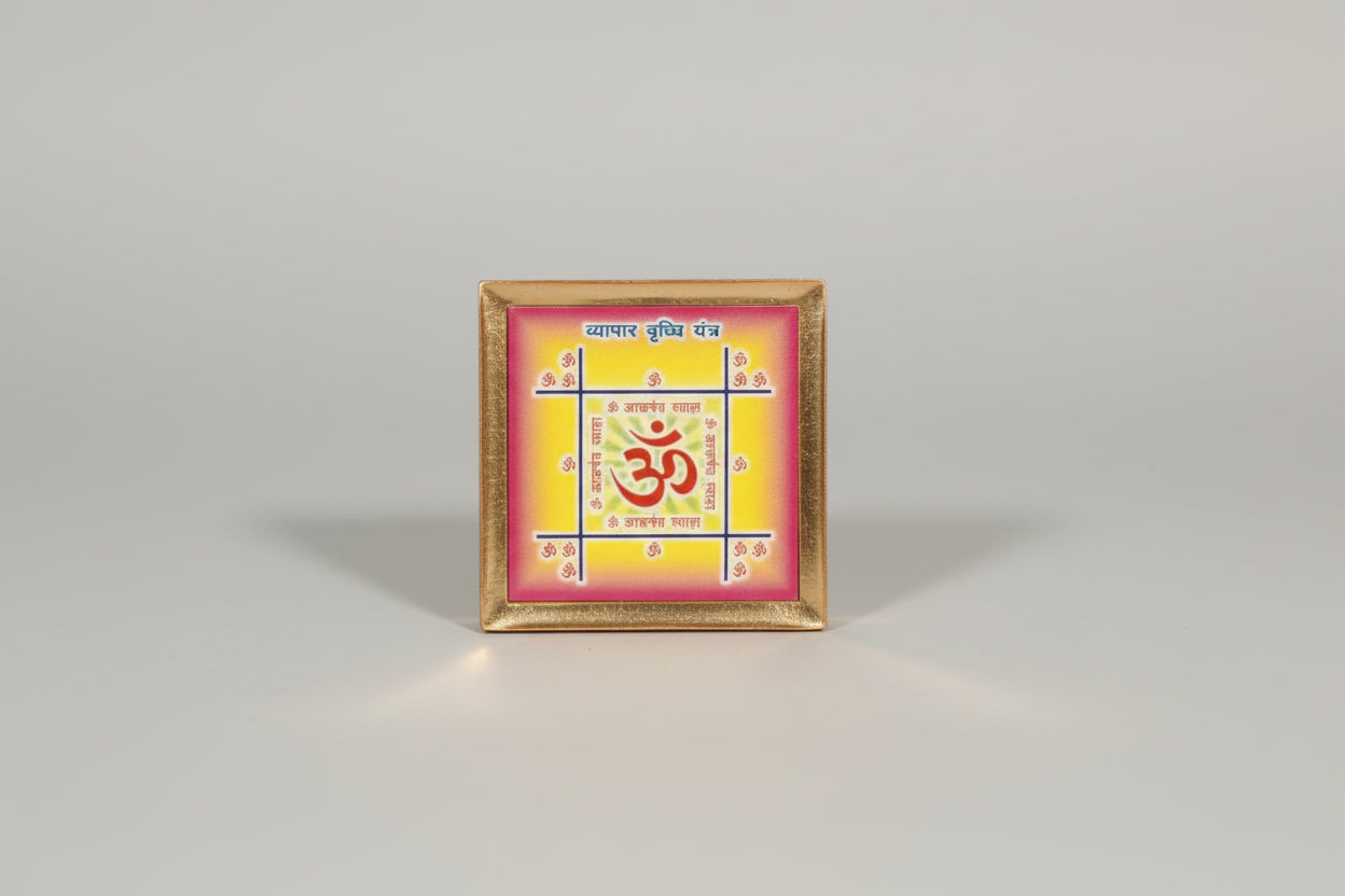 A Vyapar Vriddhi Yantra, featuring a red and yellow design with an Om symbol, held in a person's hand.