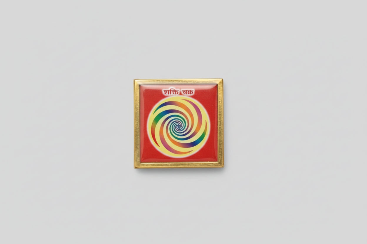 A Sarv Siddh yantra held in a person's hand, featuring a multicolored spiral design on a red background, encased in a clear plastic cover.