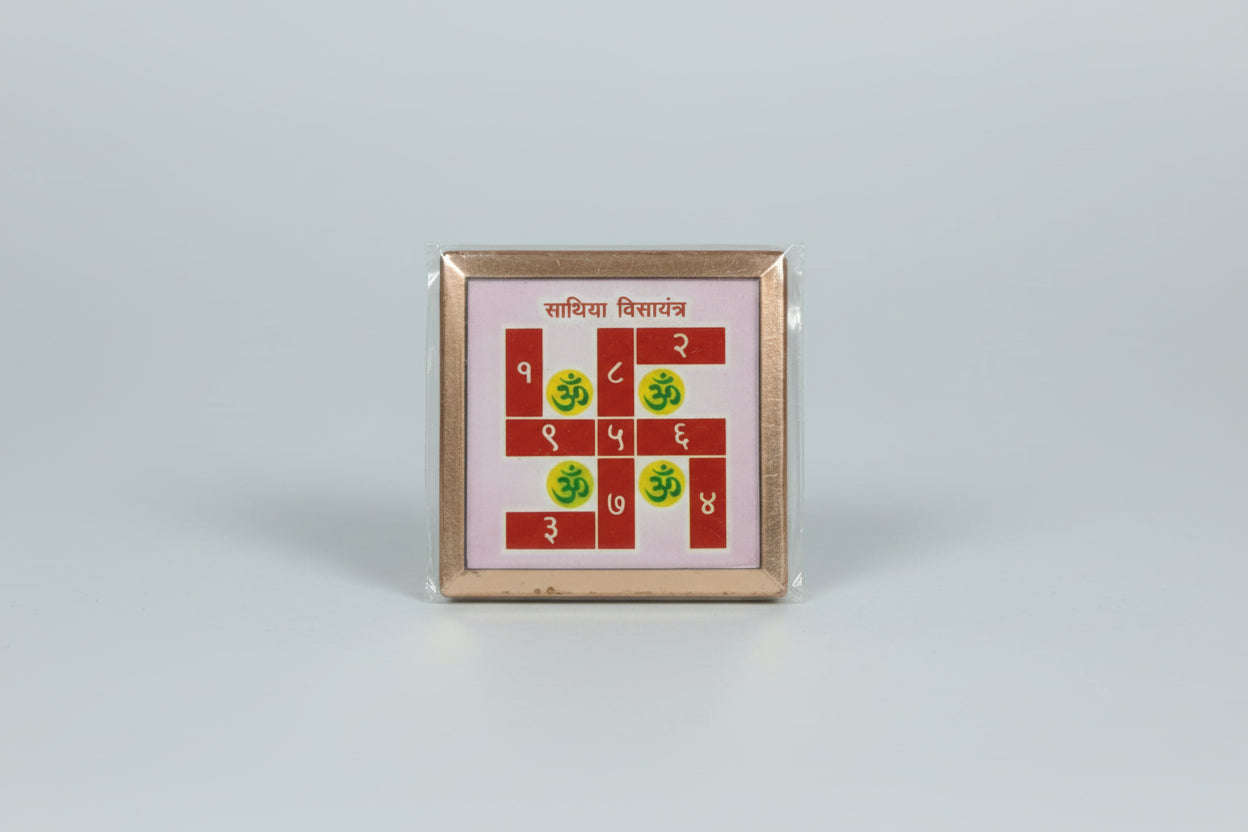 A hand holding a Swastik Yantra, a sacred Hindu symbol, against a red background with golden patterns.