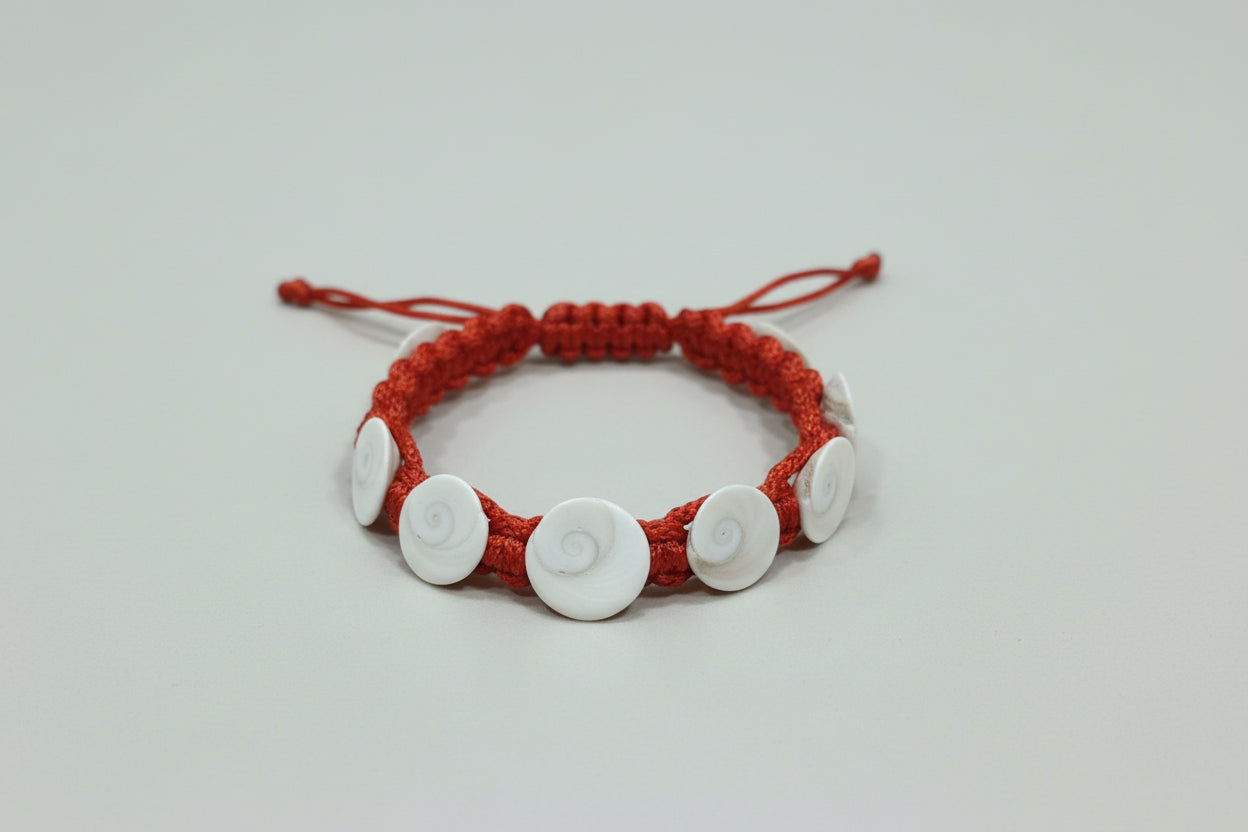 A hand holding a red bracelet with white circular pendants, featuring five Gomti chakra designs.