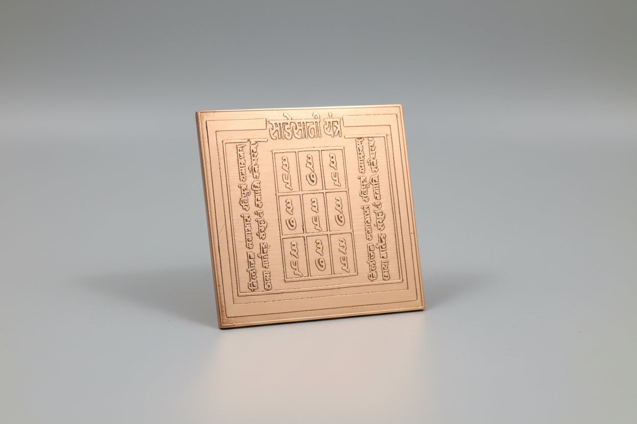 A copper colored Sade Sati Yantra with engraved text and geometric designs held in a person's hand.