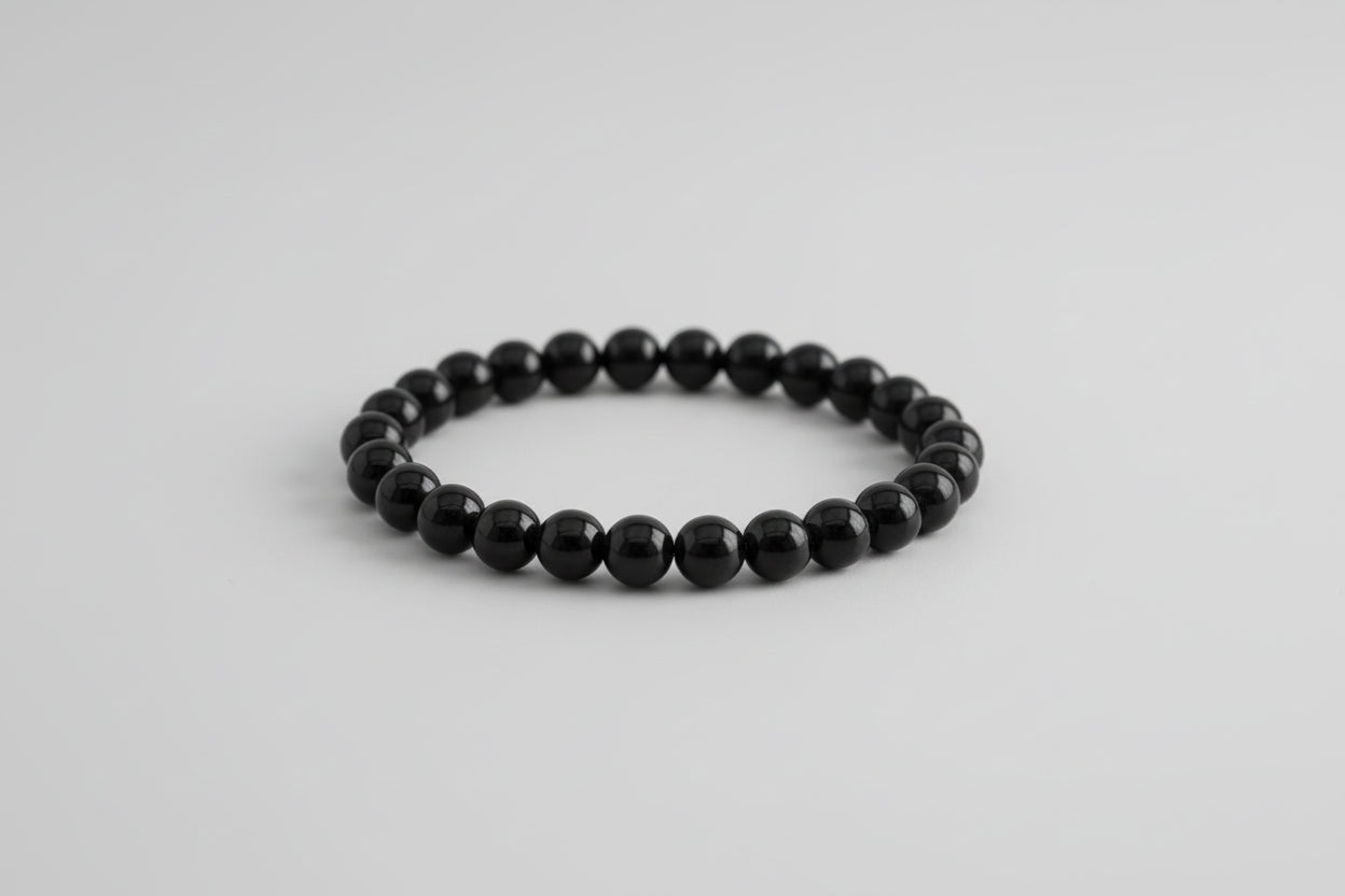 A black tourmaline bracelet displayed against a floral background with the text detailing its benefits such as shielding, grounding, and protecting the aura.