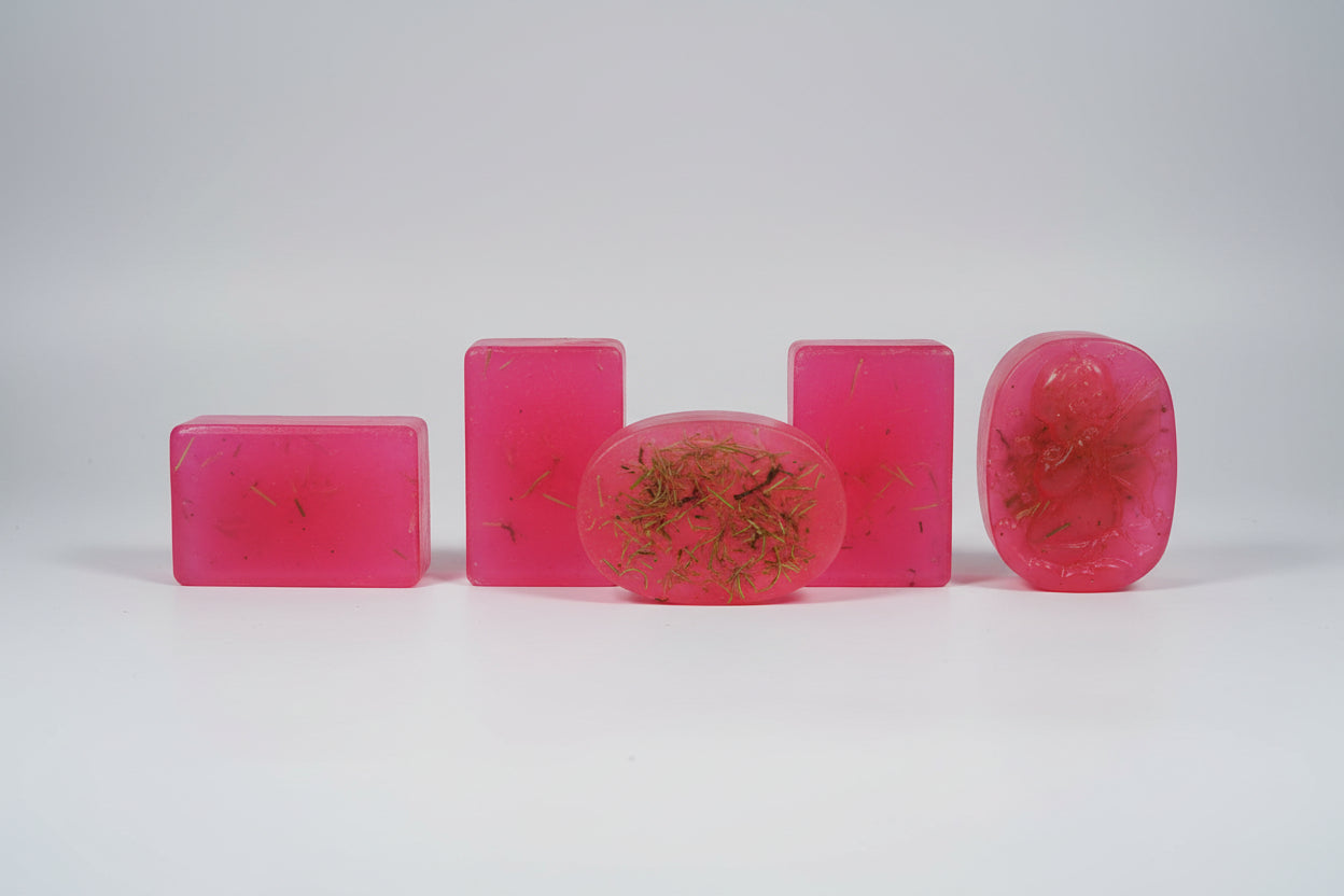 The image shows a packaged Angel Aura Cleansing Soap with a red label indicating the product name and purpose. Below the package, there's a photograph of the soap itself, which is red with visible herbs integrated into its texture.