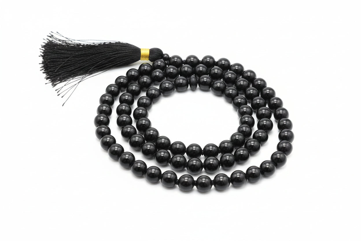 A Black Onyx Japmala with a tassel, displayed on a red background. The text on the image mentions the birthdate associated with the planet Rahu and the name of the stone.