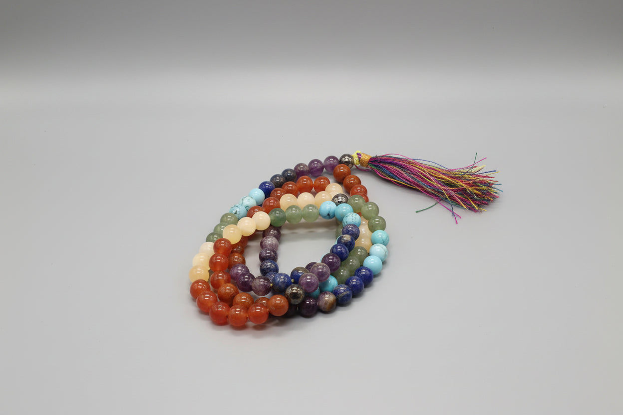 A multicolored beaded 7 chakra Japmala with a tassel, laid out on a red surface.
