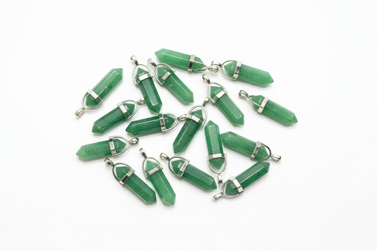 A collection of green aventurine pencil-shaped pendants with metal caps on both ends, laid out on a brown surface.