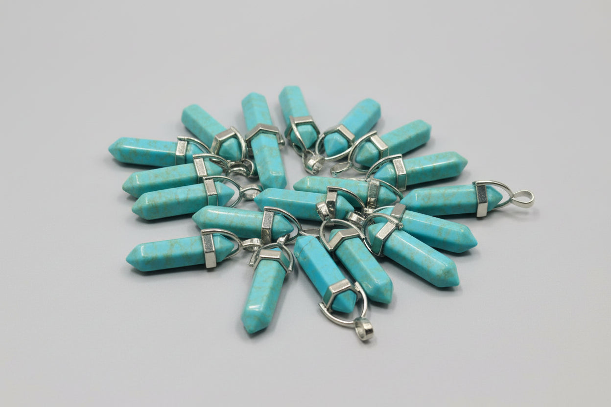 A collection of turquoise pencil-shaped pendants displayed on a textured surface.