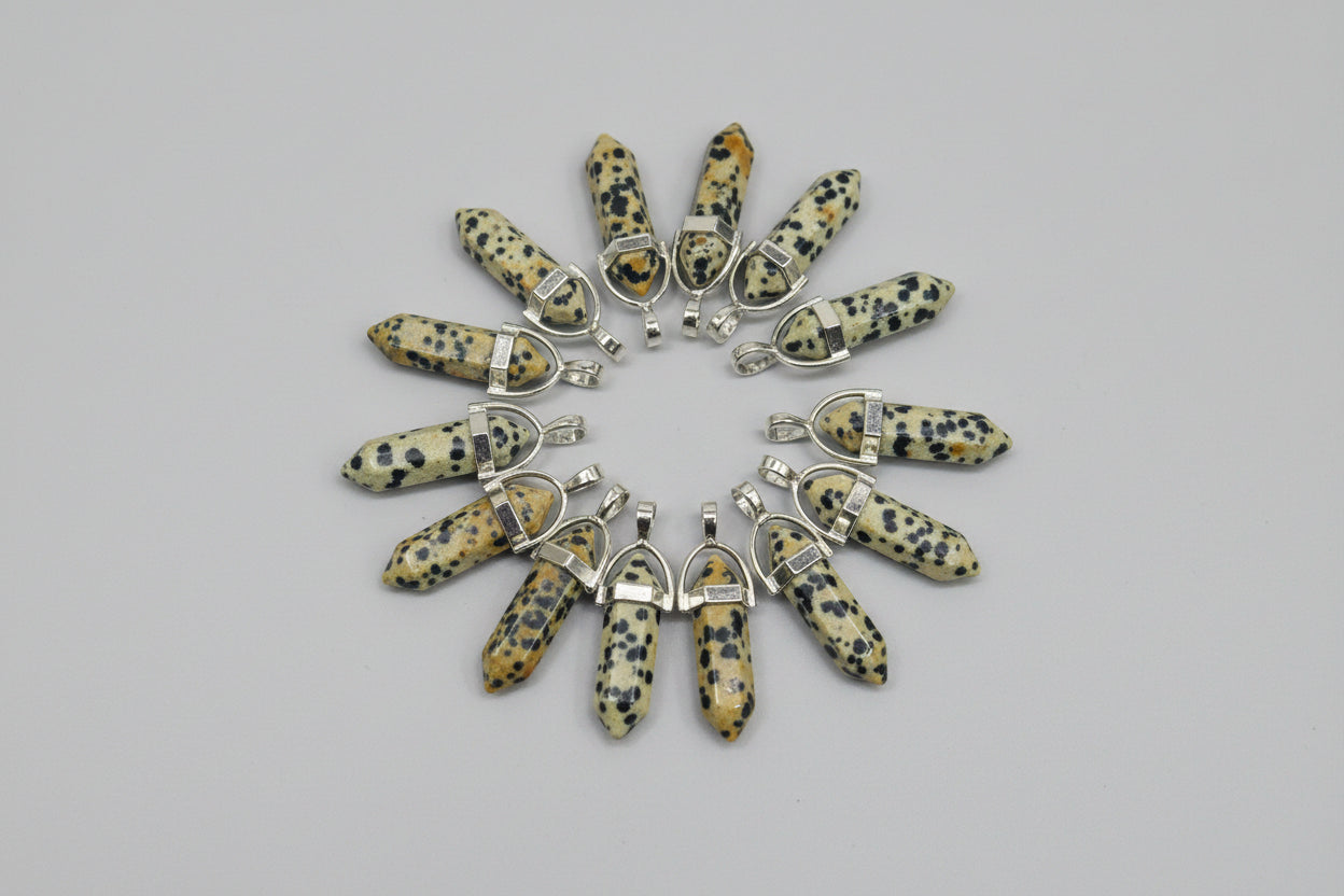 A collection of Dalmatian Jasper pencil-shaped pendants displayed on a textured brown surface.