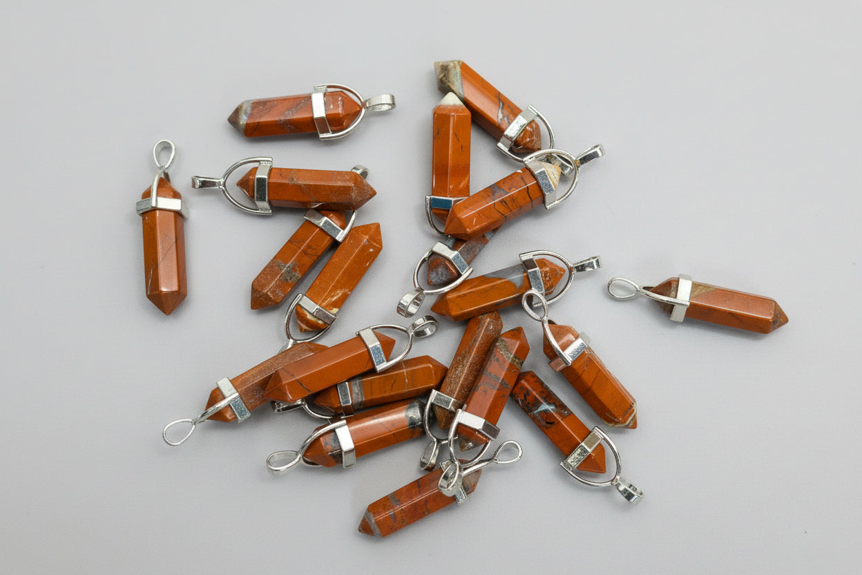 A collection of jasper pencil pendants with silver caps and loops, displayed on a textured brown surface.
