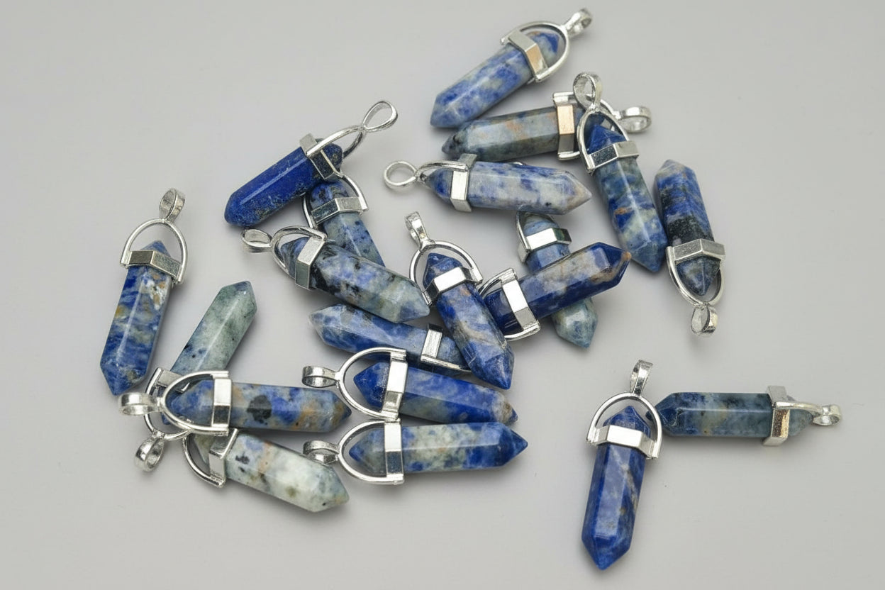 A collection of sodalite pencil pendants with metal caps on both ends, displayed on a textured background.