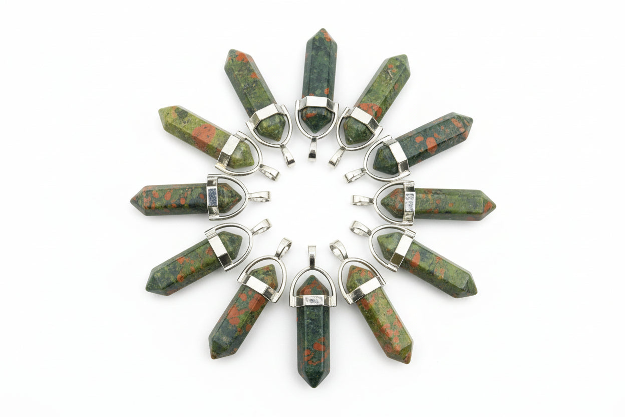 A collection of bloodstone pencil-shaped pendants with metal caps at both ends, displayed on a textured brown surface.