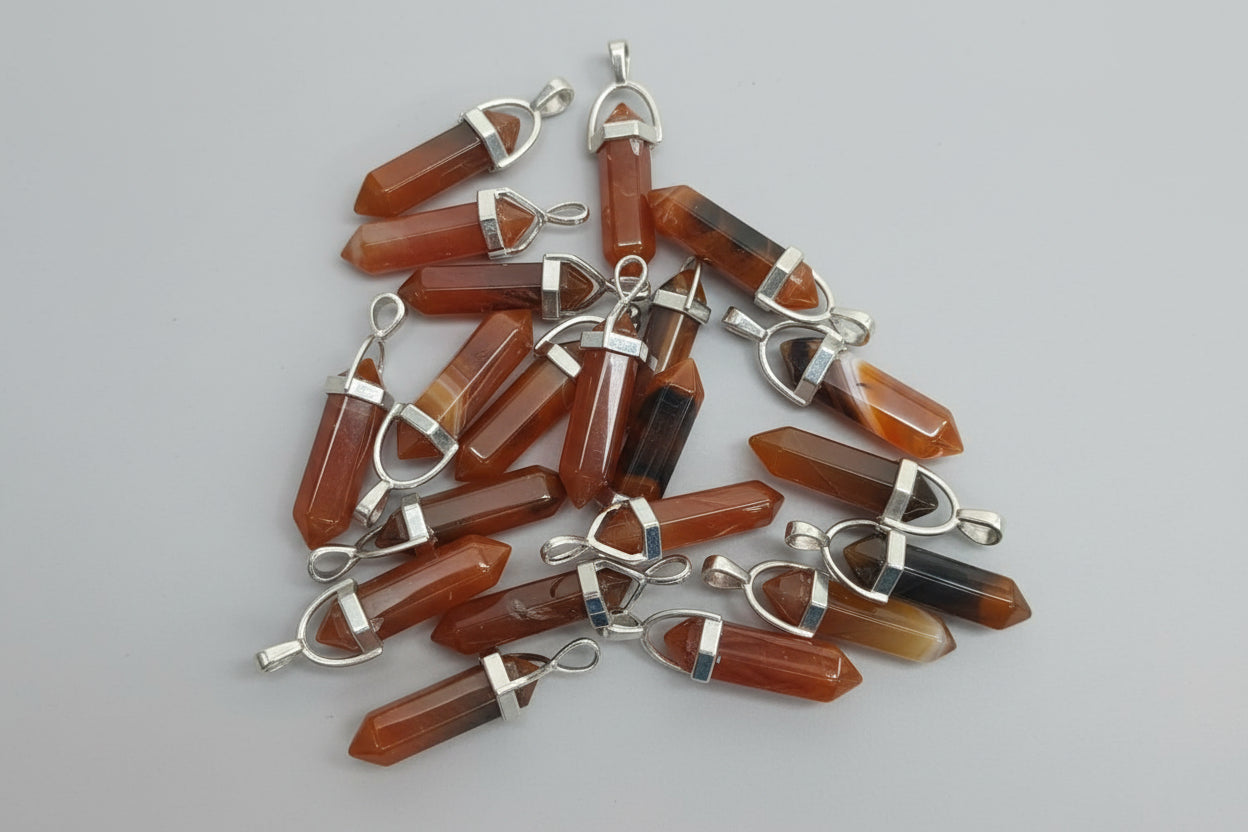 A collection of carnelian pencil pendants with silver-colored caps and loops, displayed on a textured brown surface.