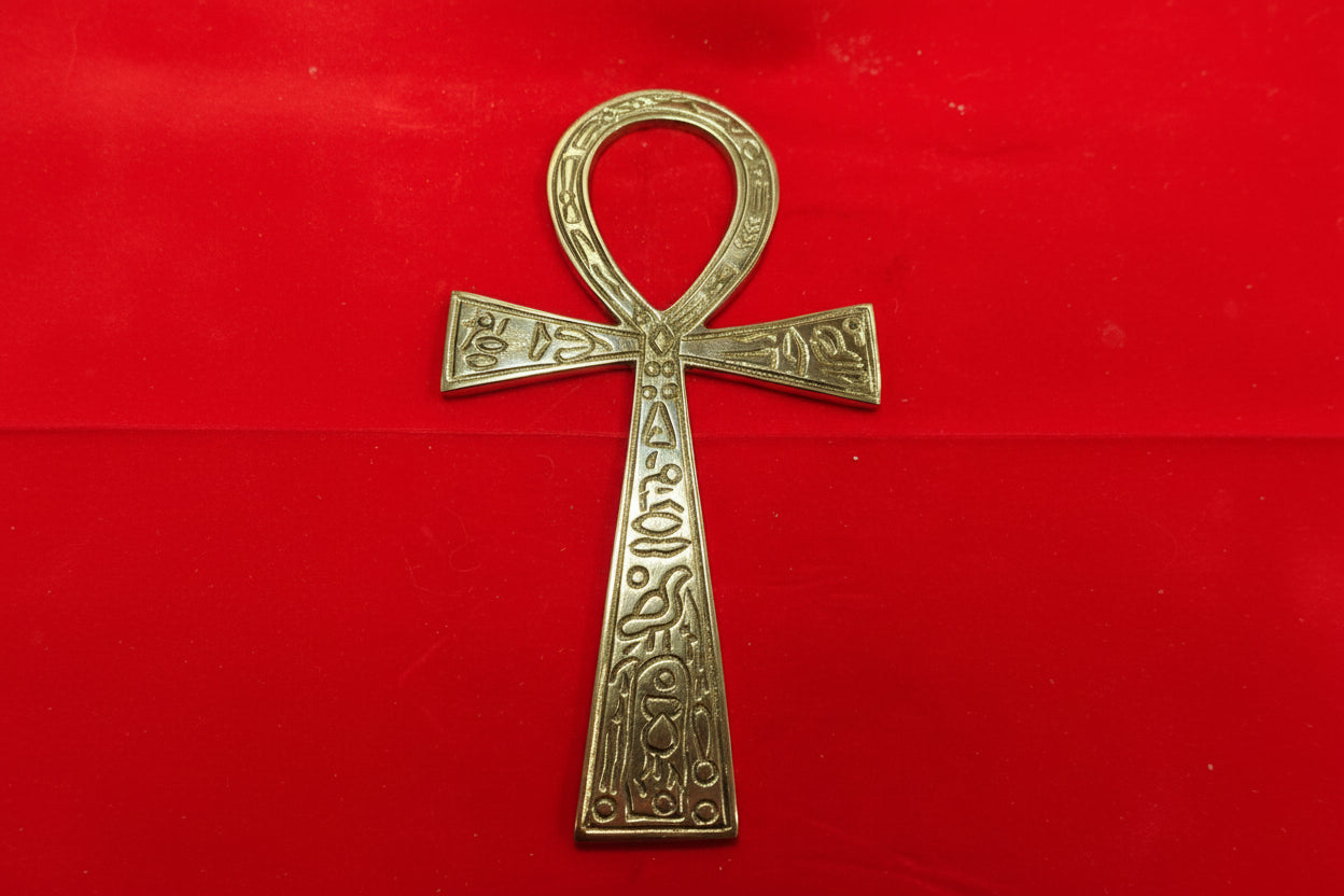 A brass ankh with intricate detailing, placed on a red background.