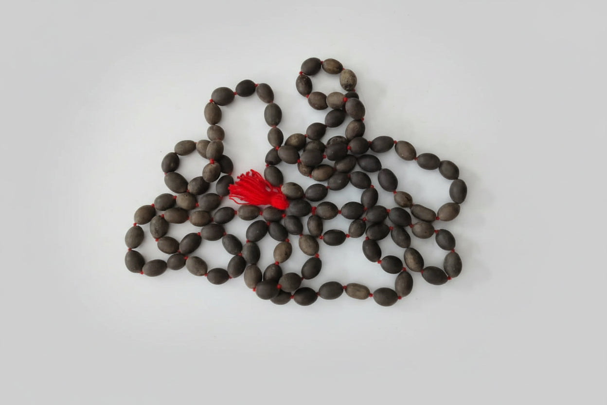 A Kamalgatha Mala with dark colored beads and a prominent red bead laid out on a surface.