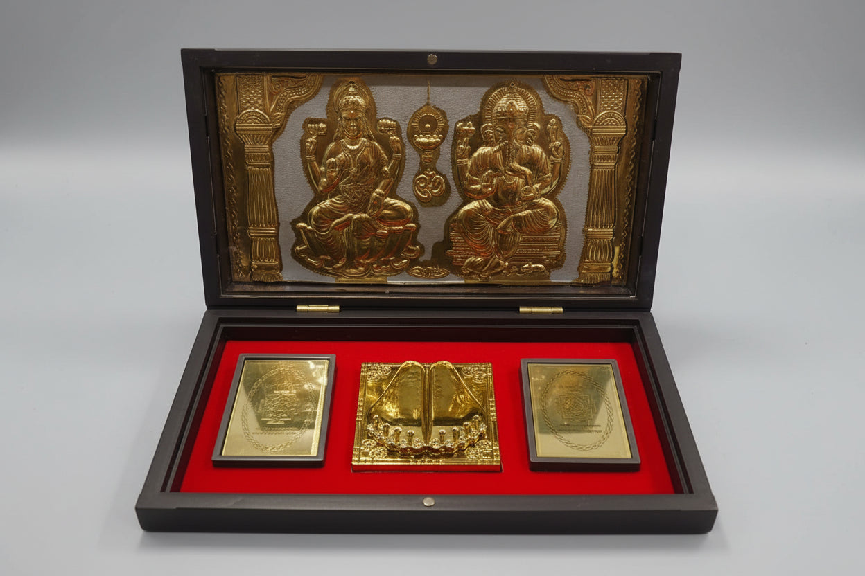 A display of spiritual items in a box, including golden idols of Maa Laxmi and Lord Ganesh, and sacred geometry symbols, placed on a red cloth.