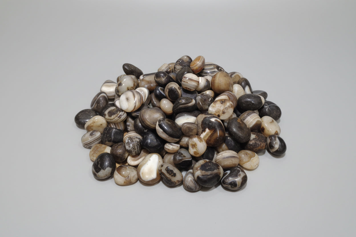 A collection of Sulemani tumble stones, also known as Black Agate, with a smooth, rounded texture and a mix of black and white colors.