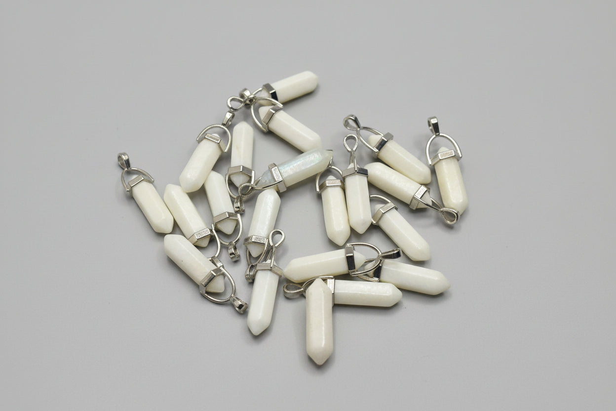 A collection of pearl shell pencil pendants with metal caps on both ends, laid out on a textured fabric surface.
