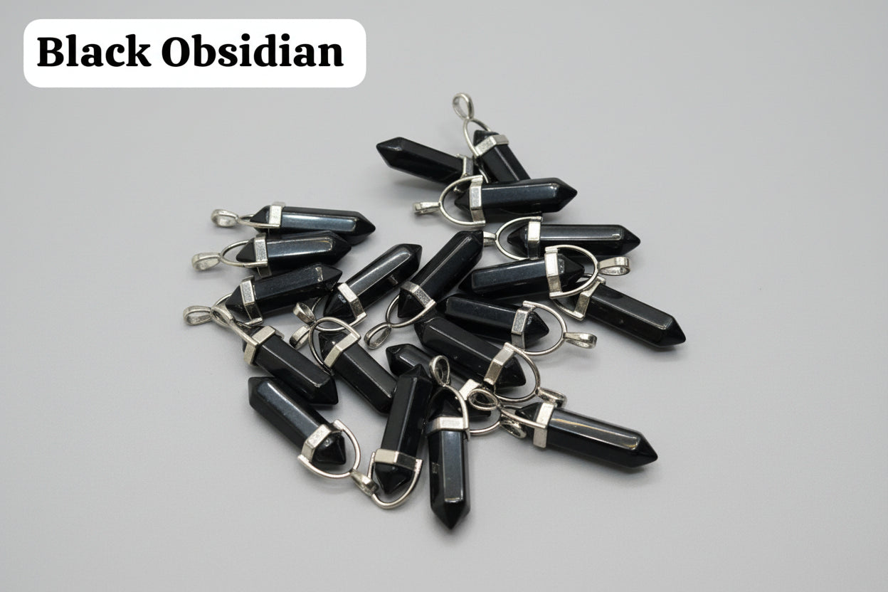 A collection of black obsidian pencil-shaped pendants with silver keychain attachments, displayed on a textured brown surface.