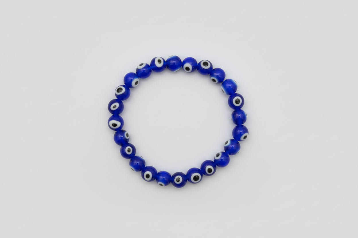 A blue bead bracelet with white and black eye patterns, displayed on a white surface with a dry leaf beside it.