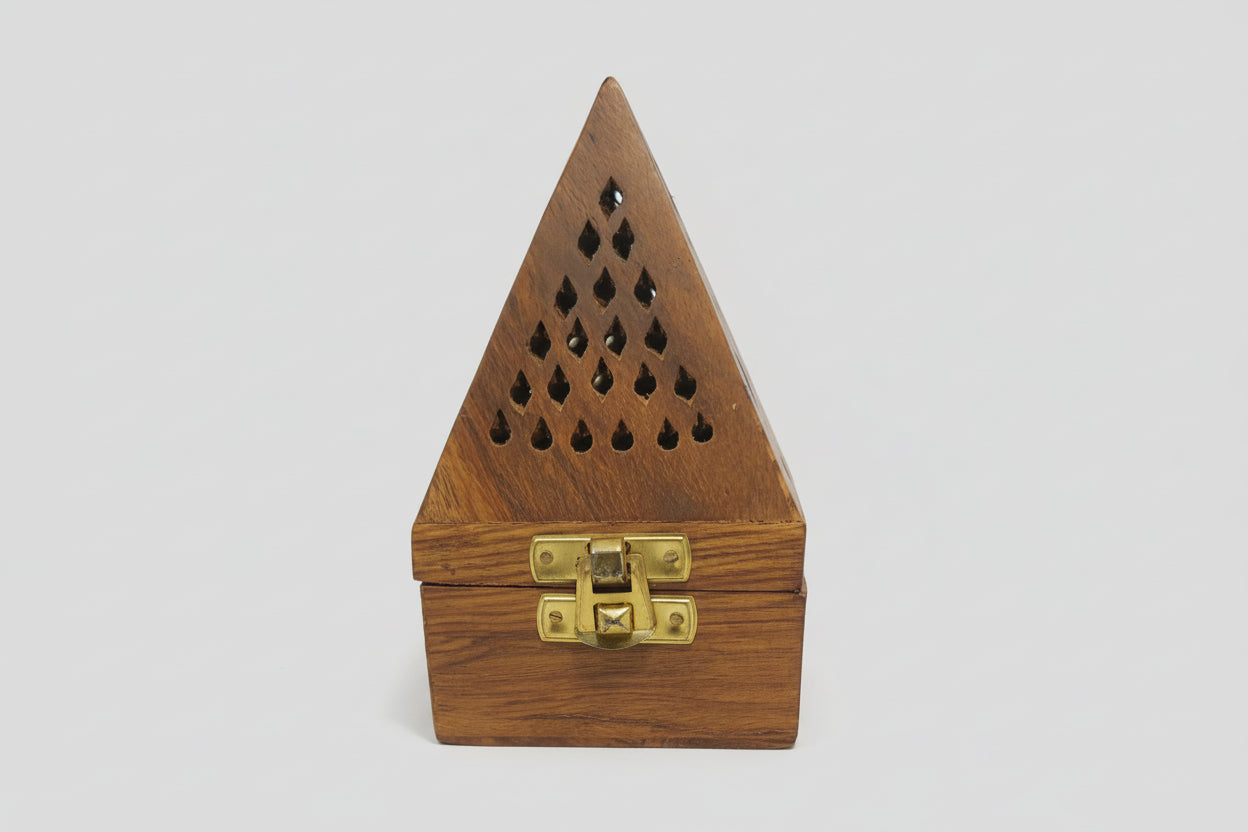A wooden dhoop dani with a triangular shape and cut-out holes on the lid, displayed on a table.