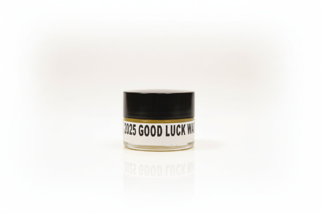 A small container labeled '2025 Good Luck wax perfume' on a wooden surface.