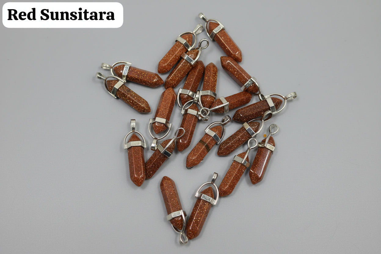 A collection of red sunstone pencil pendants with metal caps on both ends, laid out on a brown surface.