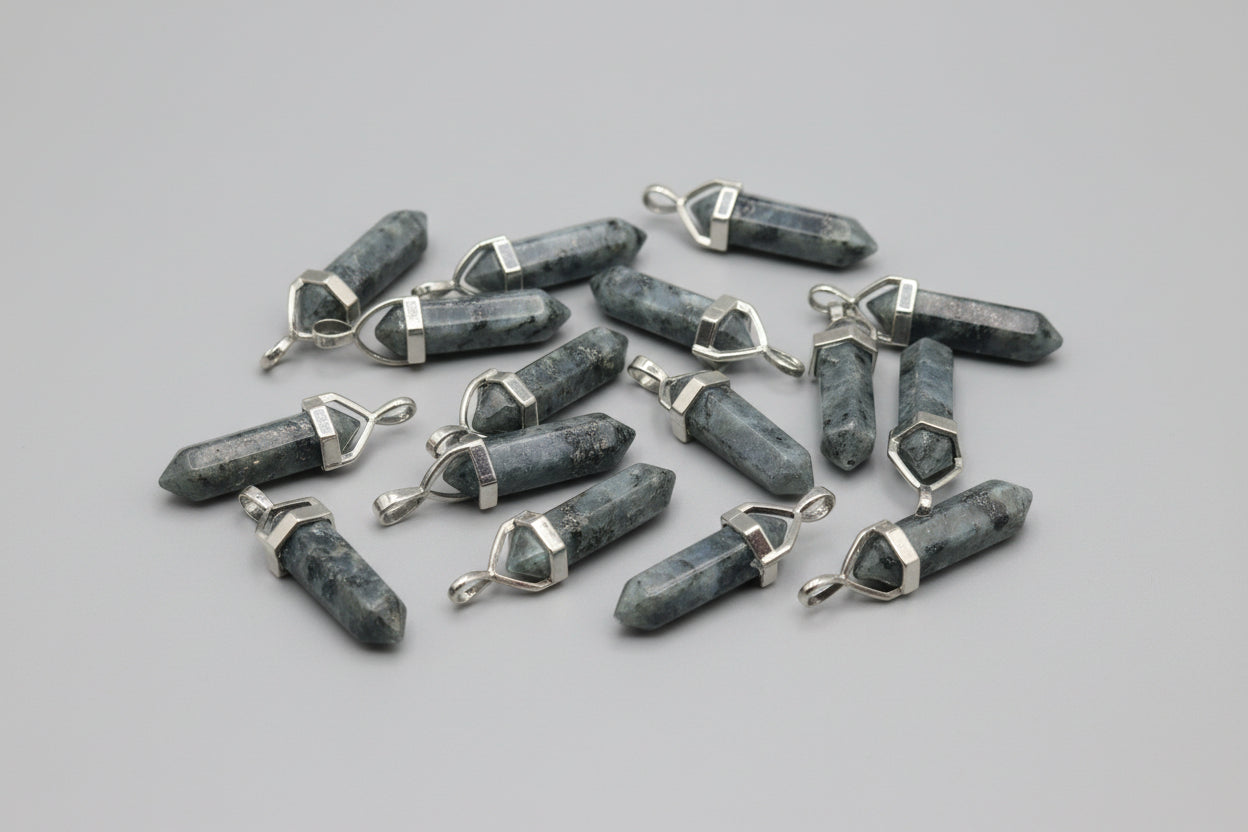 A collection of Larvikite pencil pendants with metal caps and loops, attached to a chain, displayed on a textured brown surface.