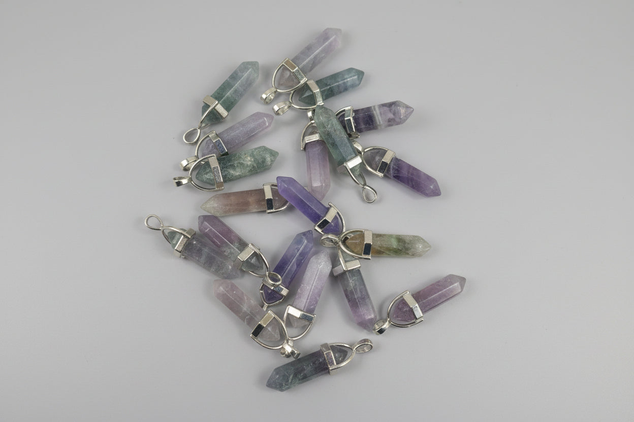 A collection of multi-colored fluorite pencil-shaped pendants displayed on a textured surface.