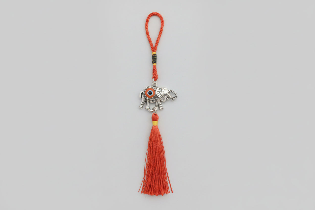 A metal elephant-shaped ornament with a silver finish and a red tassel hanging from a loop.