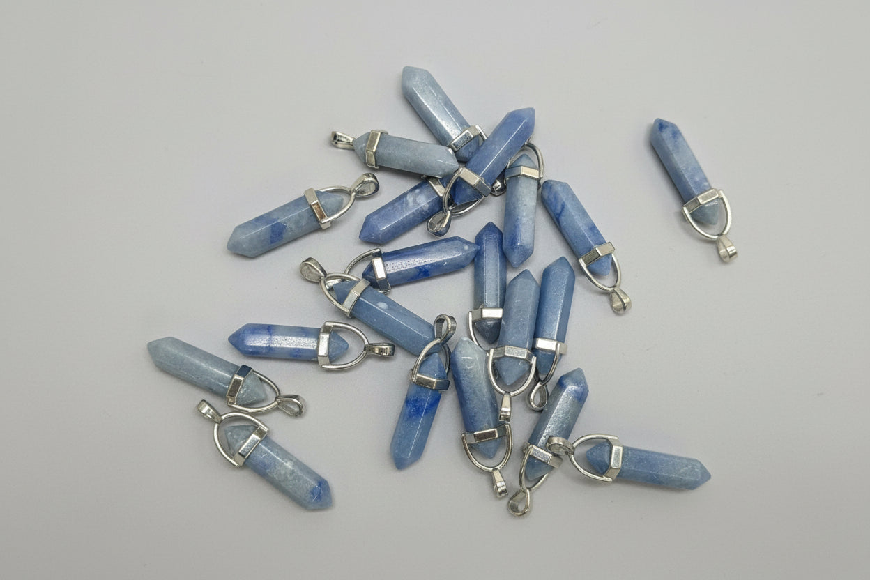 A collection of blue aventurine pencil-shaped pendants with metal clasps, placed on a textured brown surface.