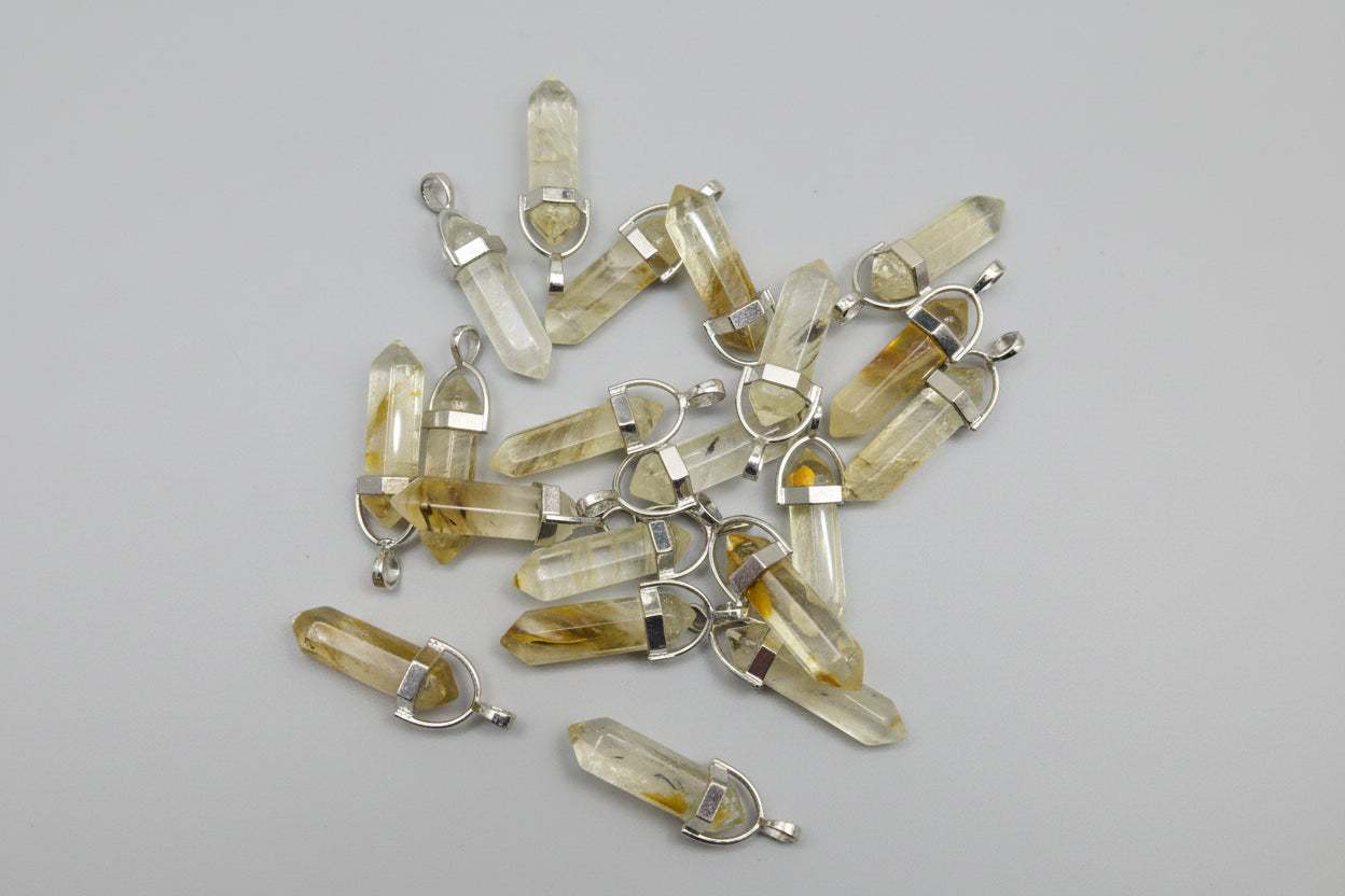 A collection of golden healer quartz pencil pendants with metal caps, attached to a loop and arranged on a textured surface.