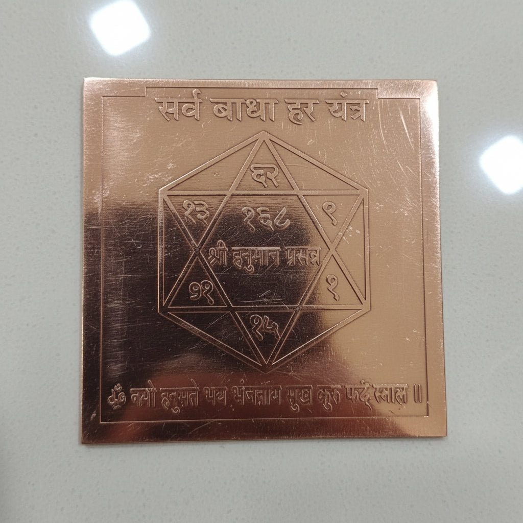 A copper-colored square yantra with geometric shapes and Hindu script engraved on it, held in a person's hand.