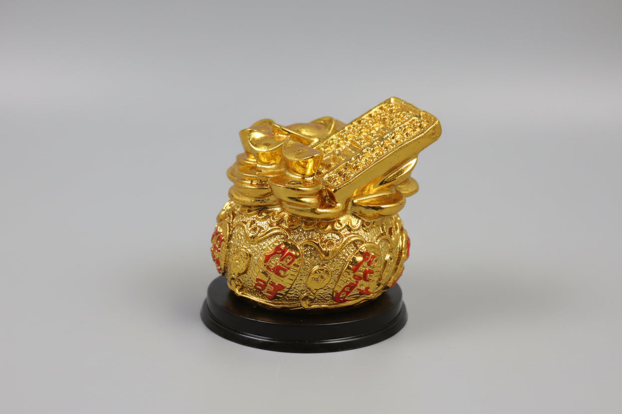 A gold-colored decorative wealth vase on a wooden surface, featuring intricate patterns and placed on a black round base.