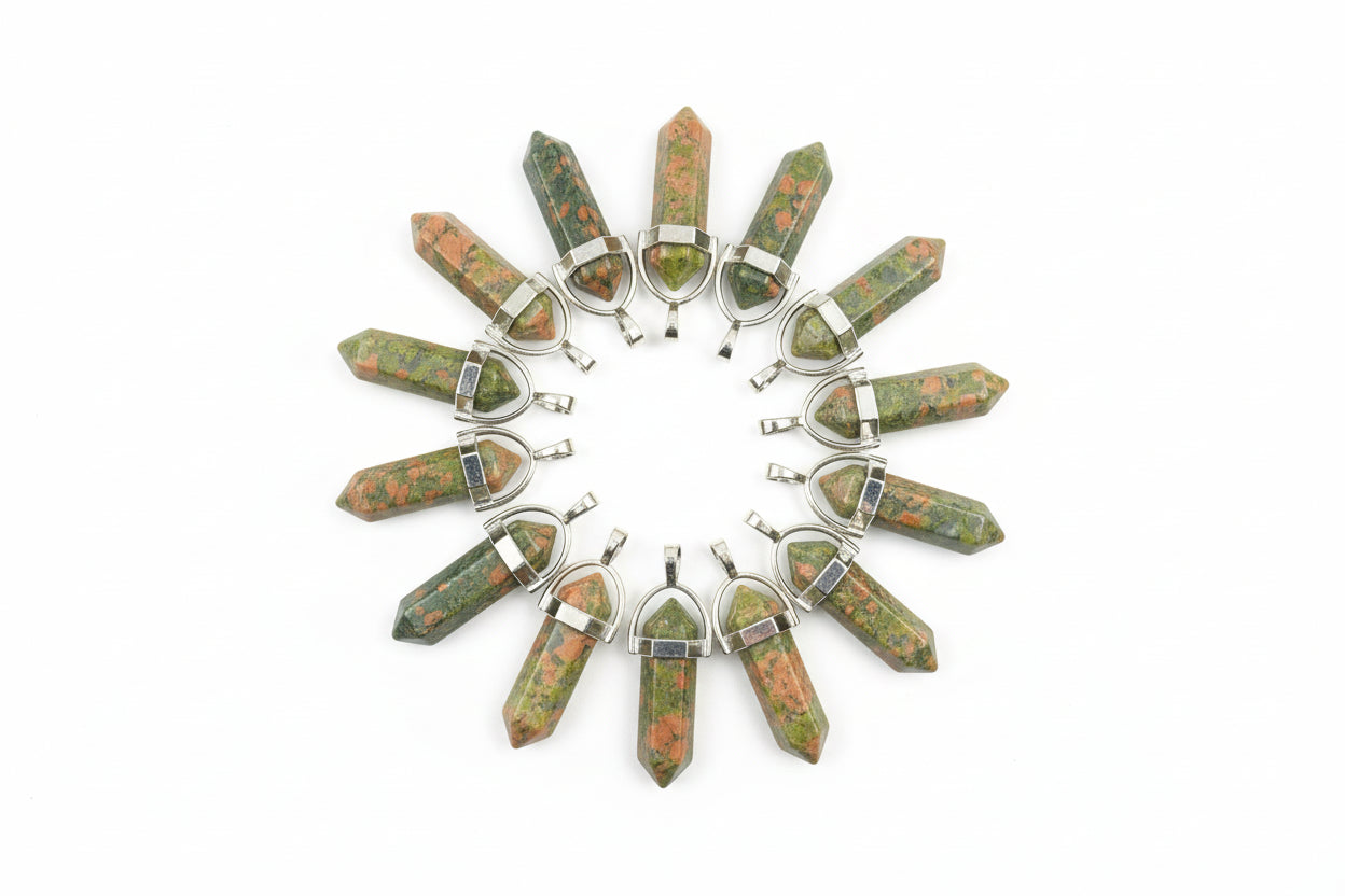 A collection of unakite pencil-shaped pendants displayed on a textured surface.